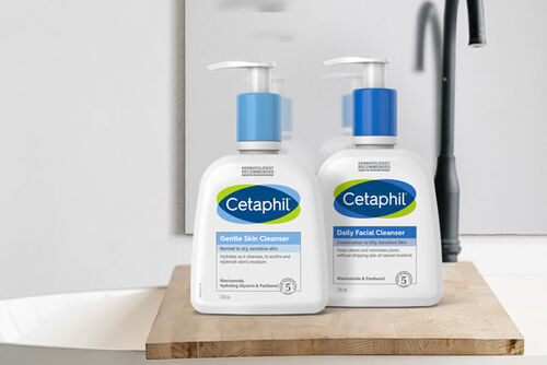 En flaske Cetaphil Gentle Skin Cleanser og en flaske Cetaphil Daily Facial Cleanser som står ved siden av hverandre på en treoverflate