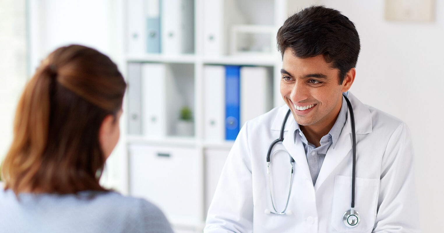 En smilende mannlig lege snakker med en pasient
