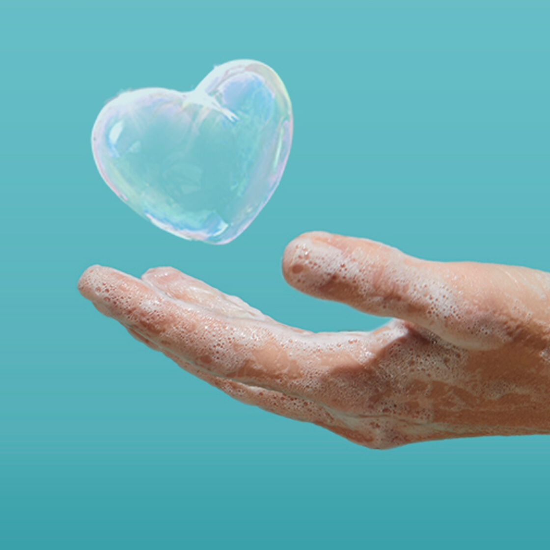 En hånd dekket av såpe, med en såpeboble formet som et hjerte som flyter fra den